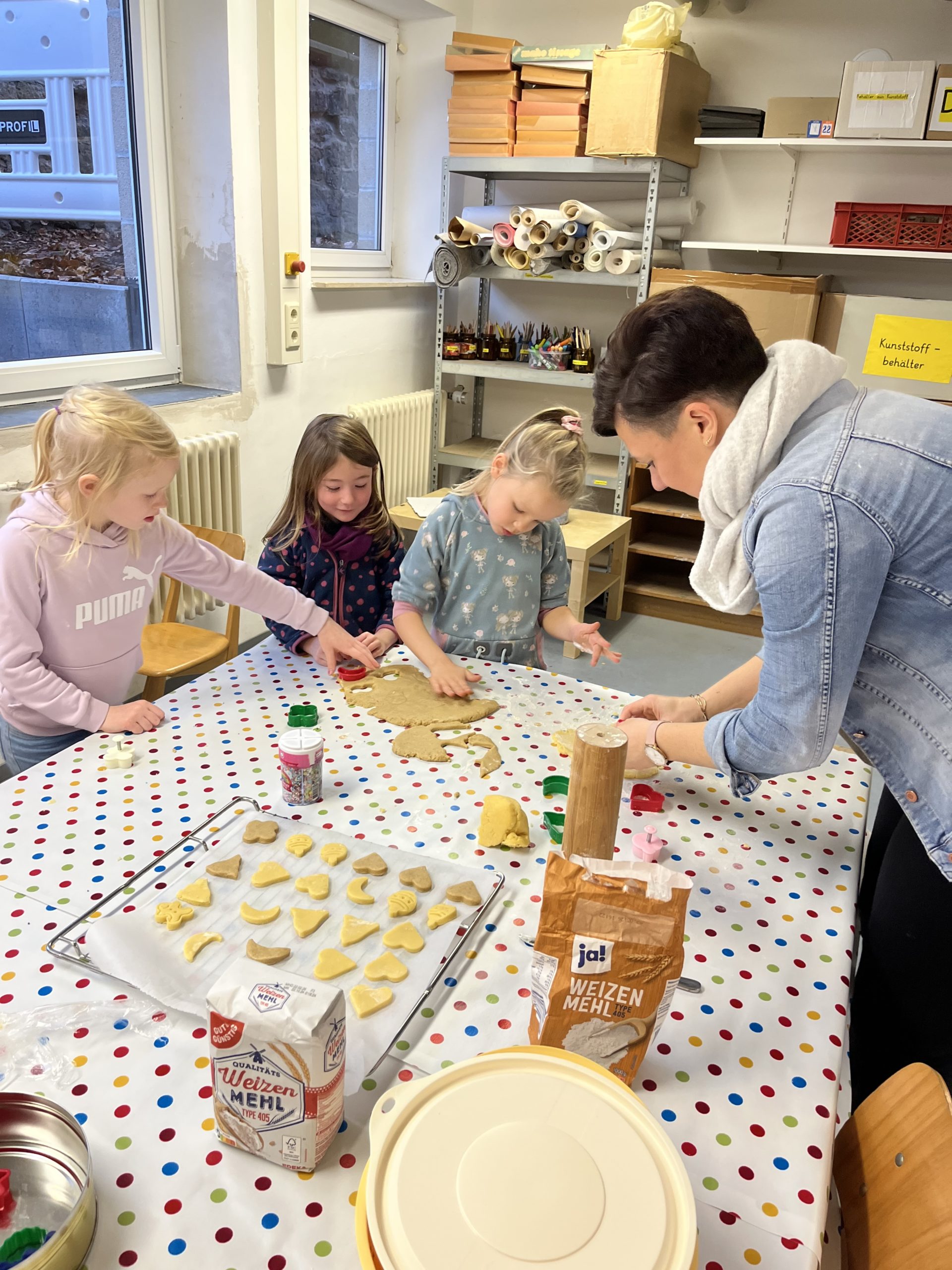Drei Mädchen stechen mit einer Mutter im Kunstkeller Plätzchen aus.